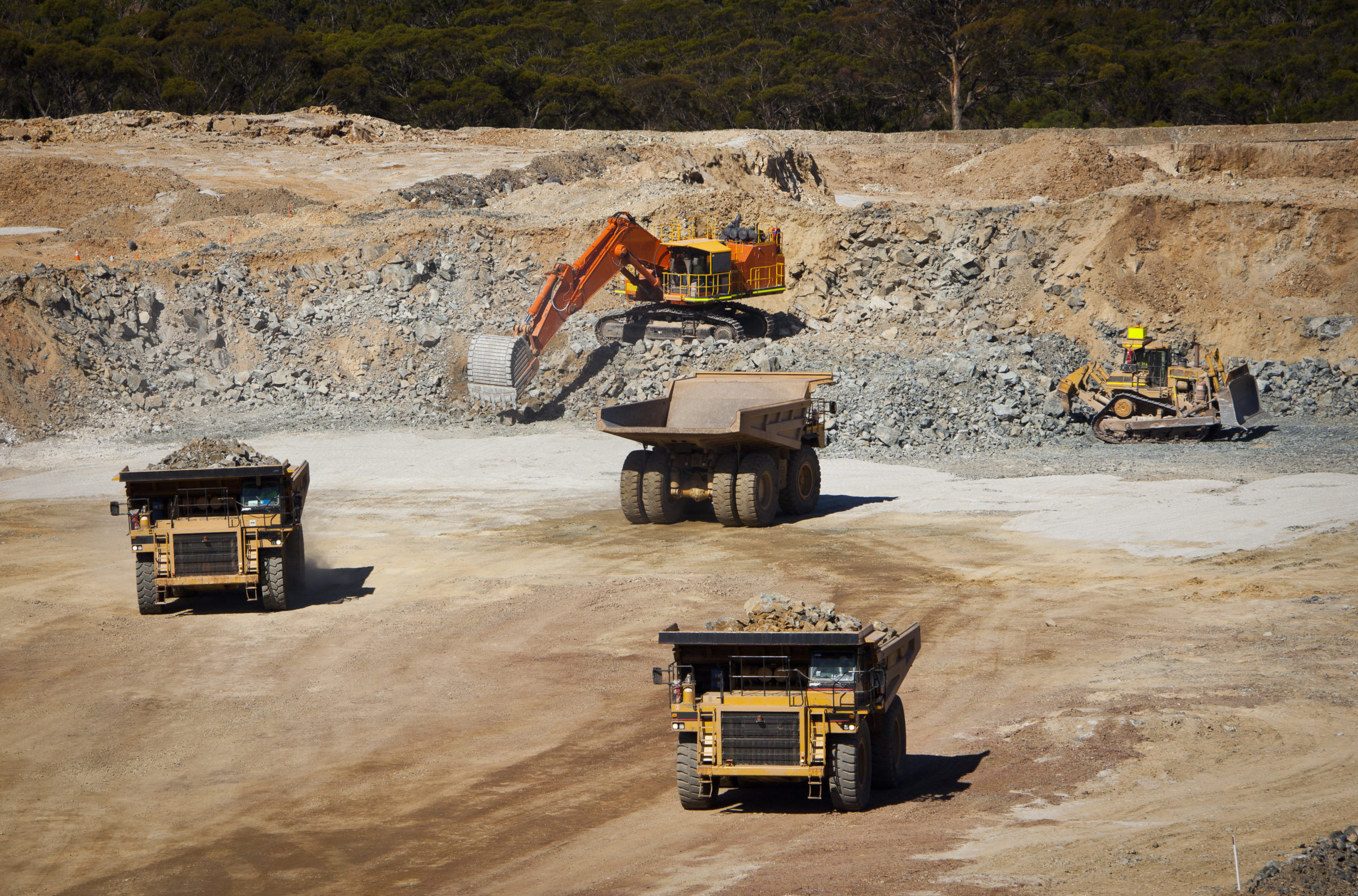 Large yellow trucks used in modern mine Western Australia. Bulldozer moves rock towards digger which fills trucks which transport ore from the open cast mine.