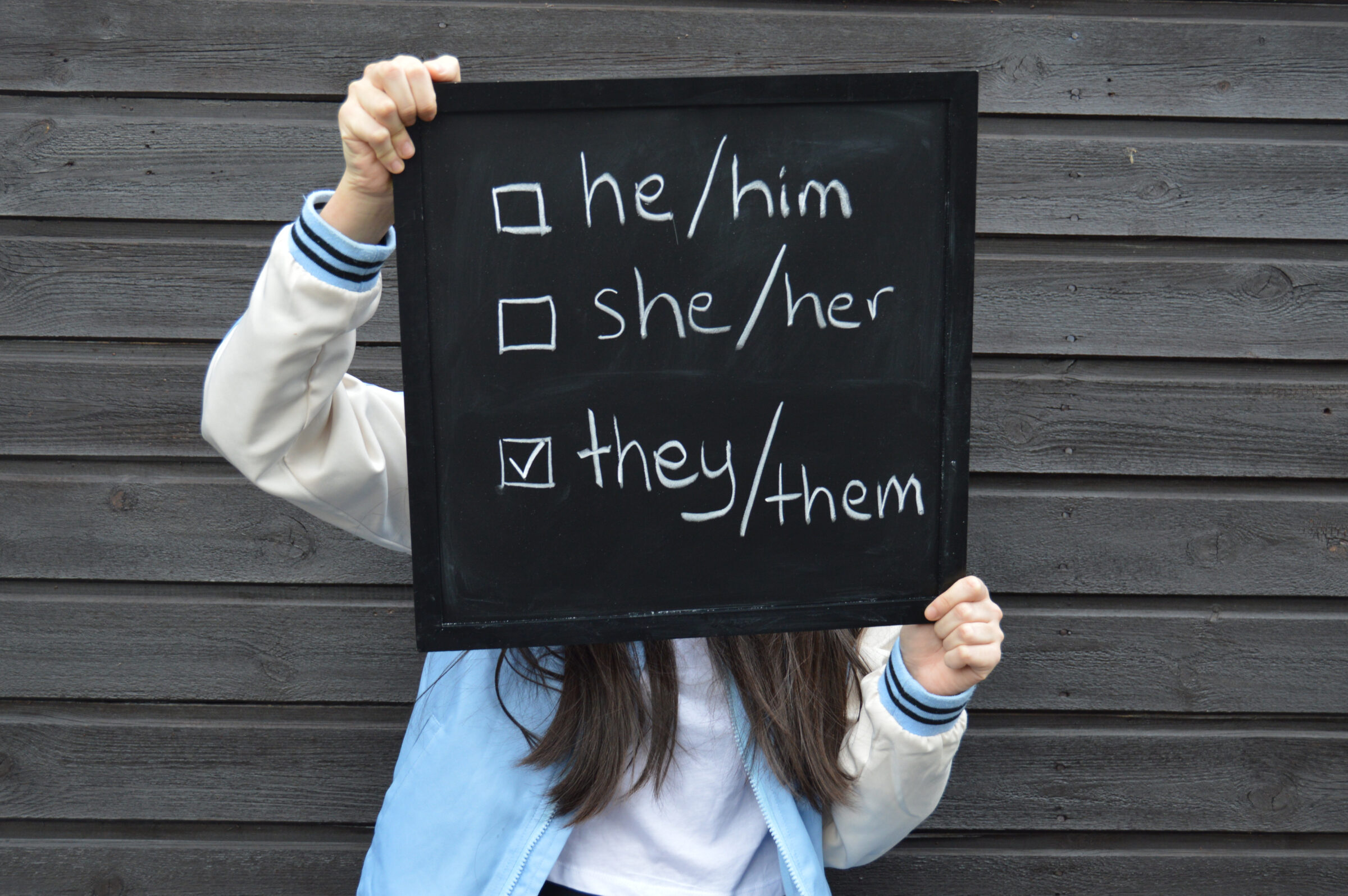 Teenager with a black board showing selection for gender identity pronouns - male, female and non-binary options