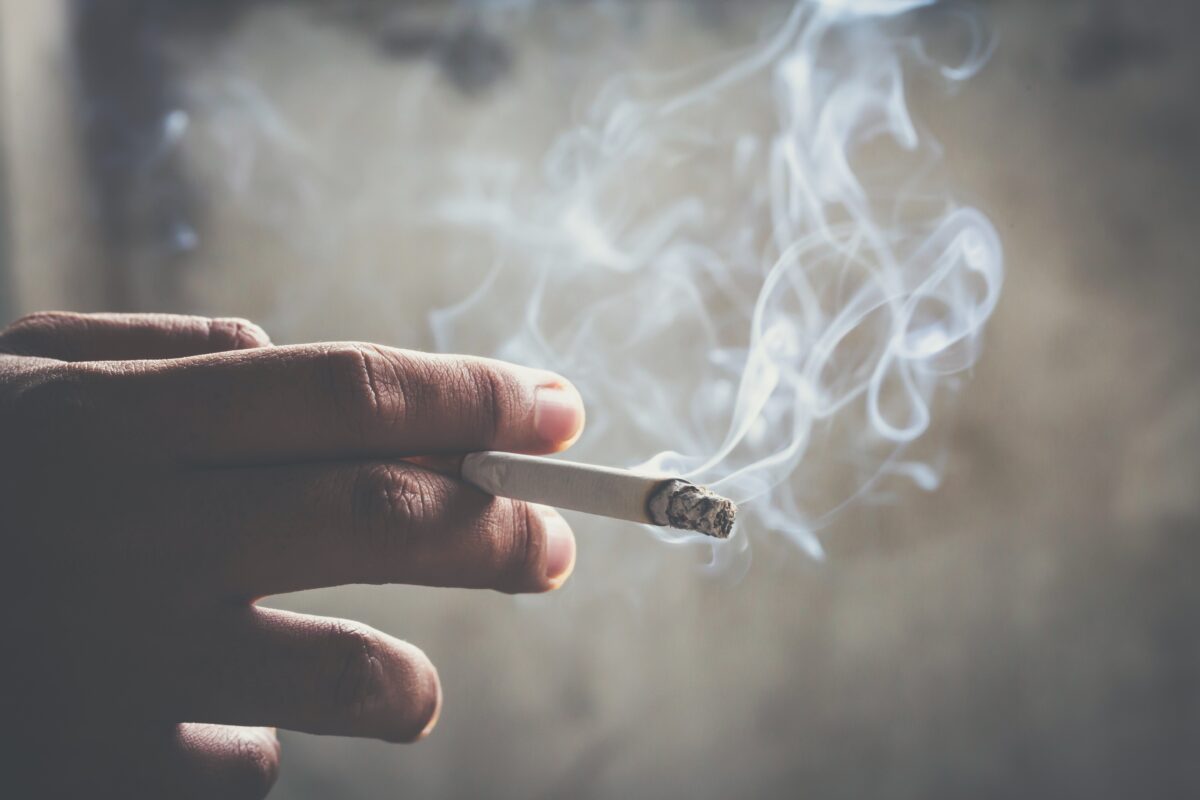 man holding smoking a cigarette in hand. Cigarette smoke spread. dark background