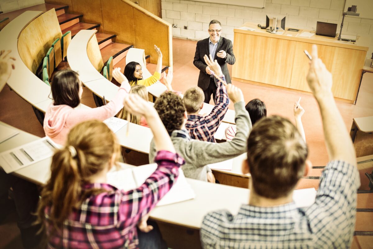 Students raising hands with teacher in lecture hall