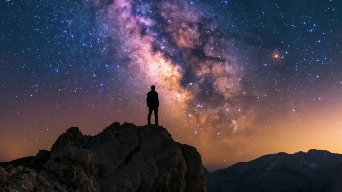 Amidst the breathtaking mountain landscape, a solitary figure stands atop a rock, gazing up at the twinkling stars in the vast night sky, mesmerized by the endless possibilities of the universe
