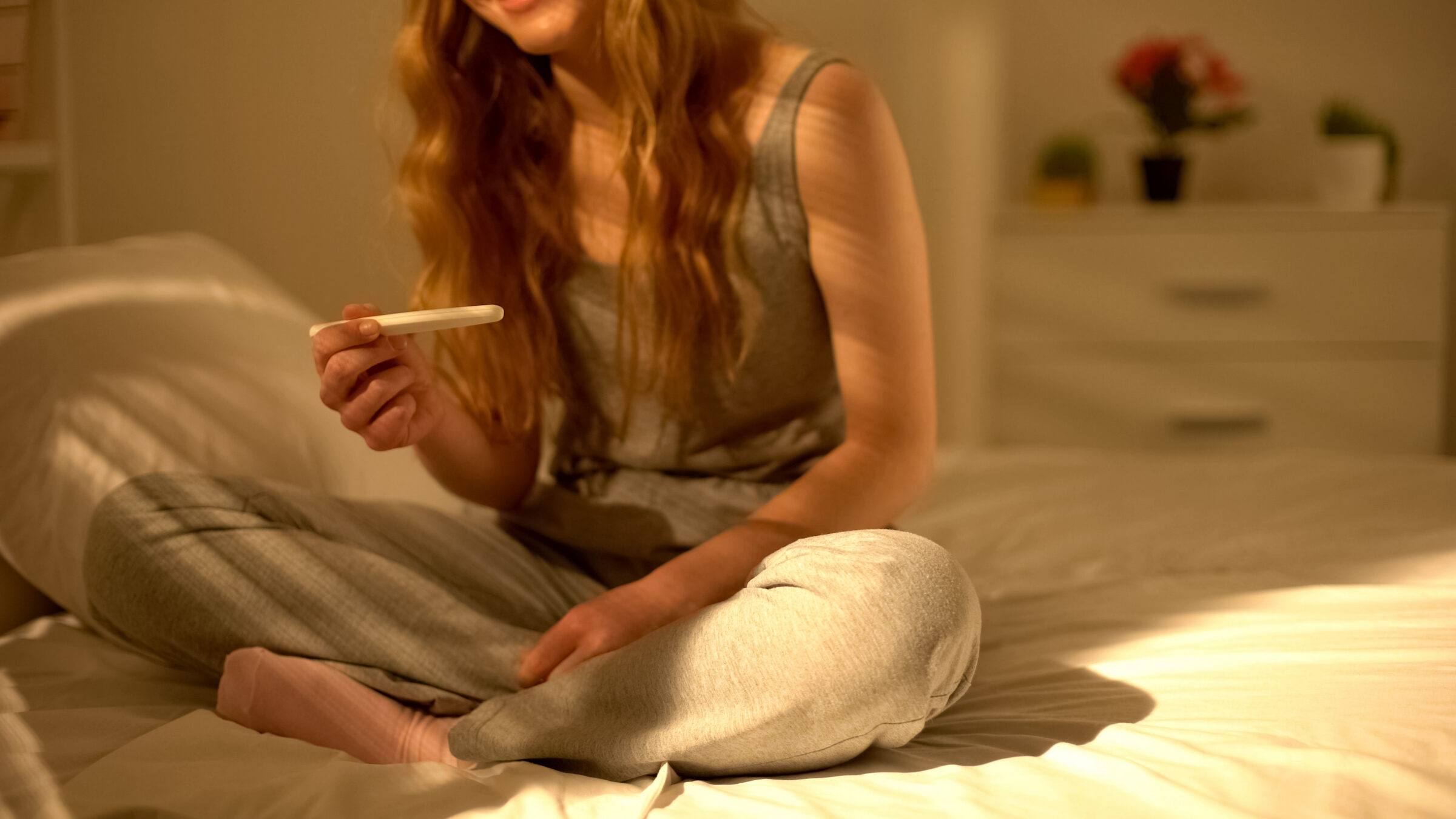 Young woman holding pregnancy test and looking at acceptable result, control