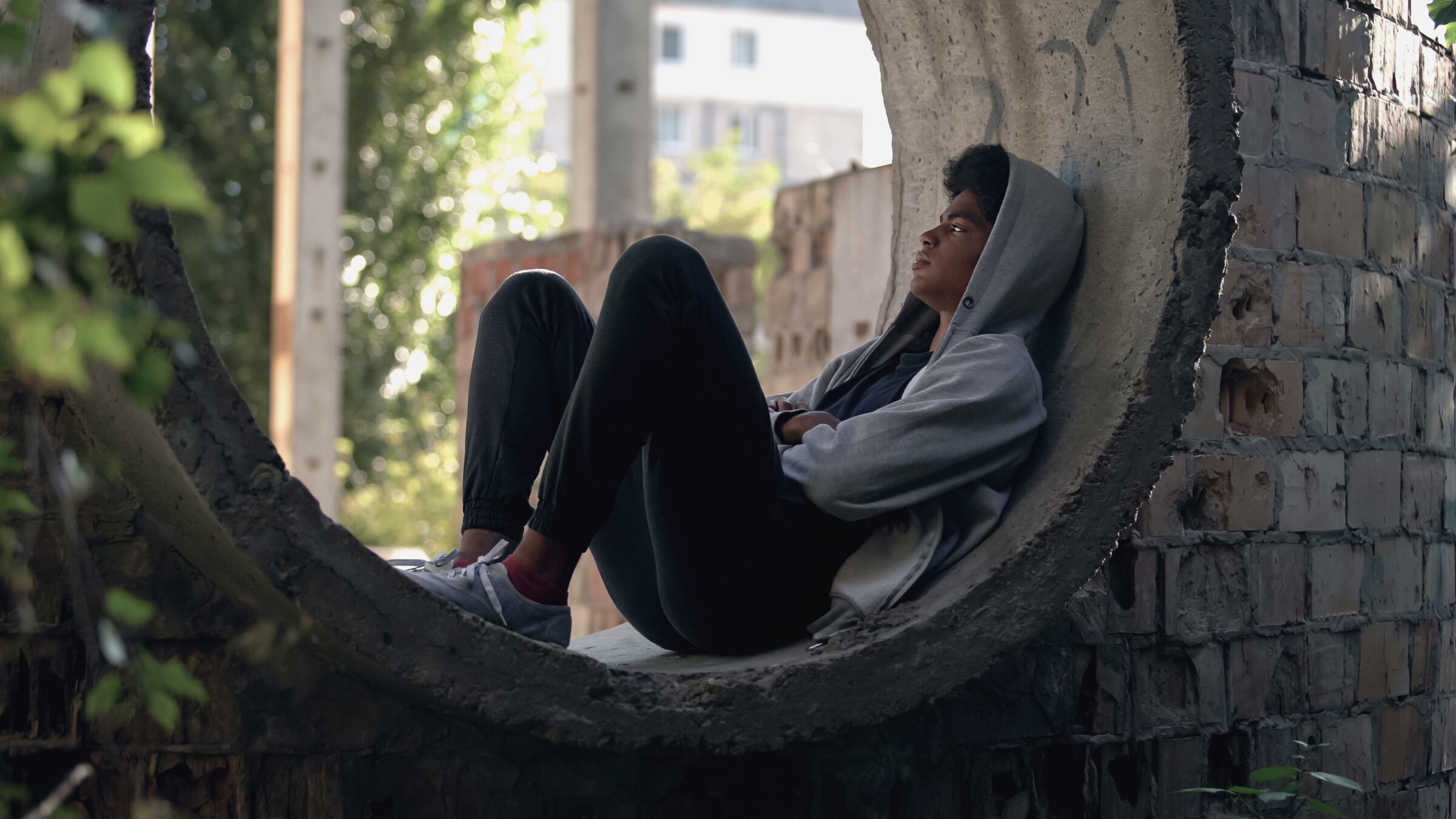 Sad lonely student in hoodie sitting alone abandoned building, puberty isolation